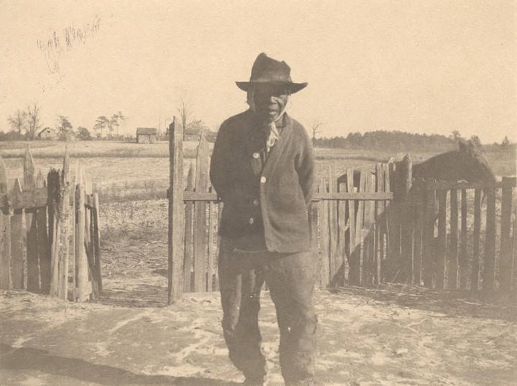 African American man standing in front of a picket fence in Crawford, Alabama.Q5586.